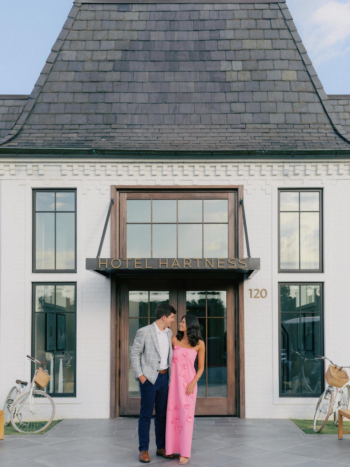 Couple posing in front of a white hotel entrance, woman wearing pink dress.