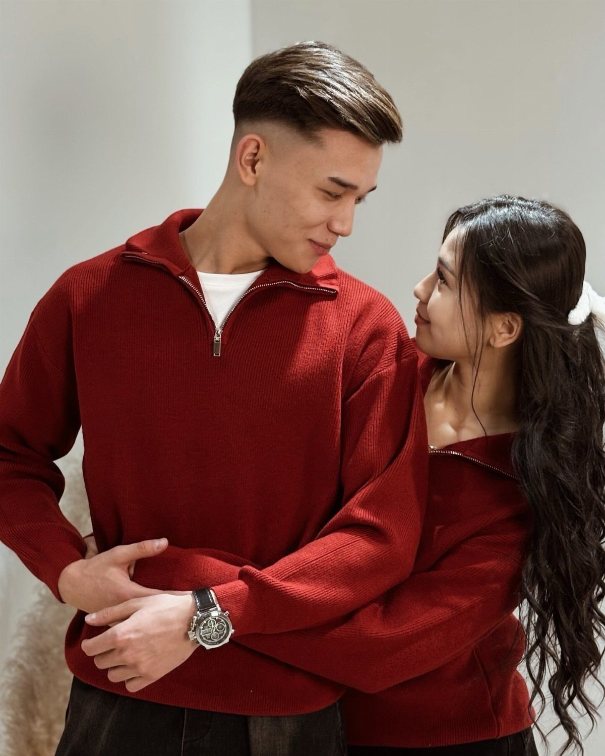 Couple wearing matching red quarter-zip pullovers posing closely against a light background.