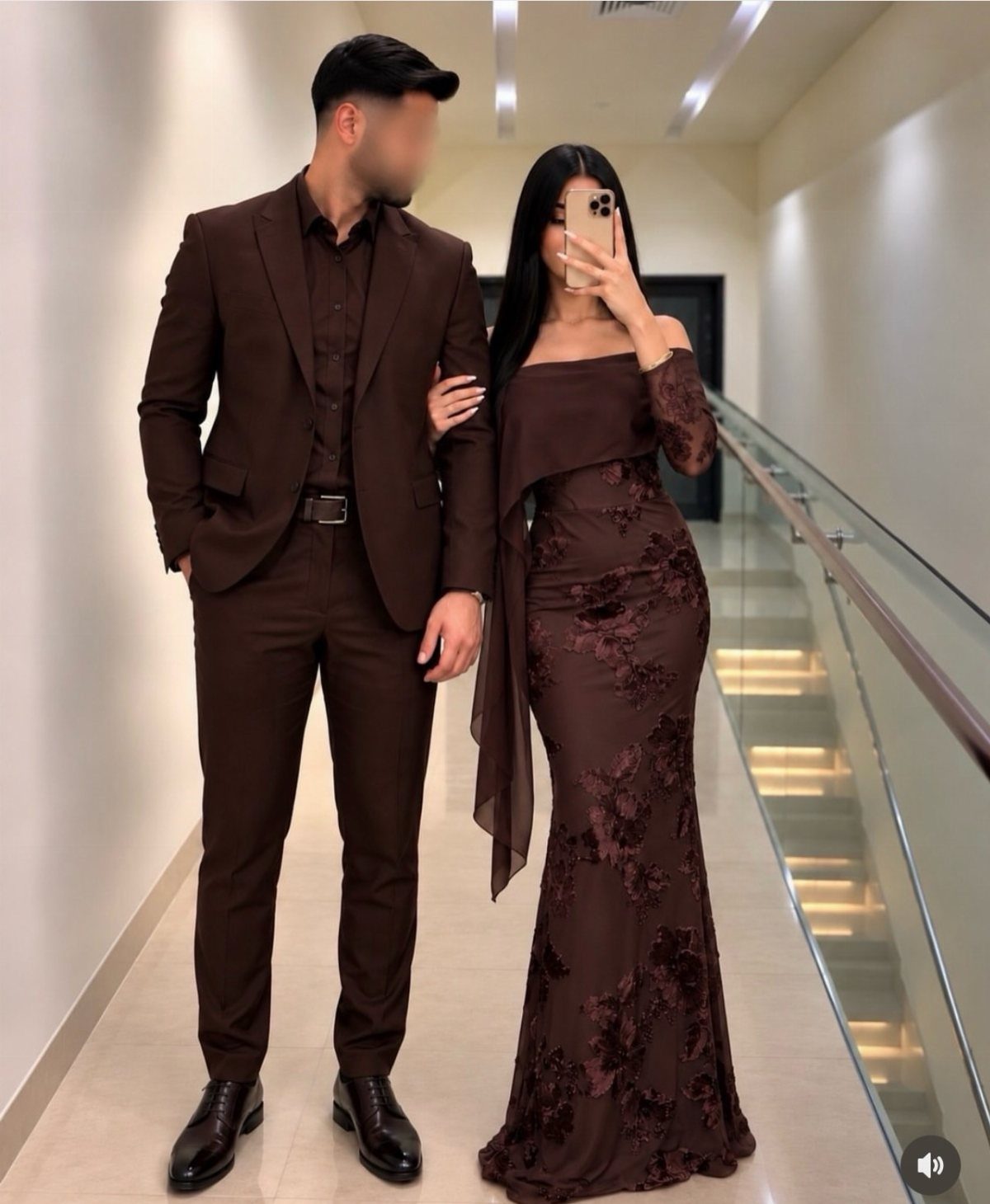 Couple wearing coordinated dark brown formal attire posing in a modern hallway