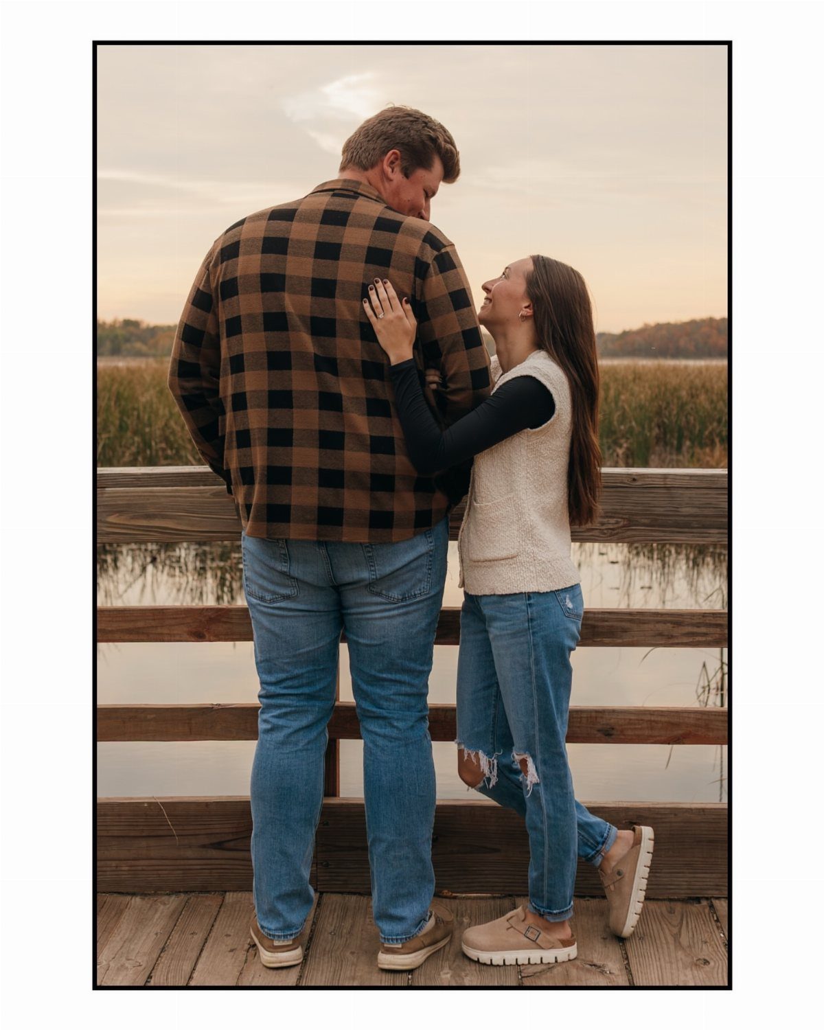 Couple in fall outfits posing on a wooden dock by a lake
