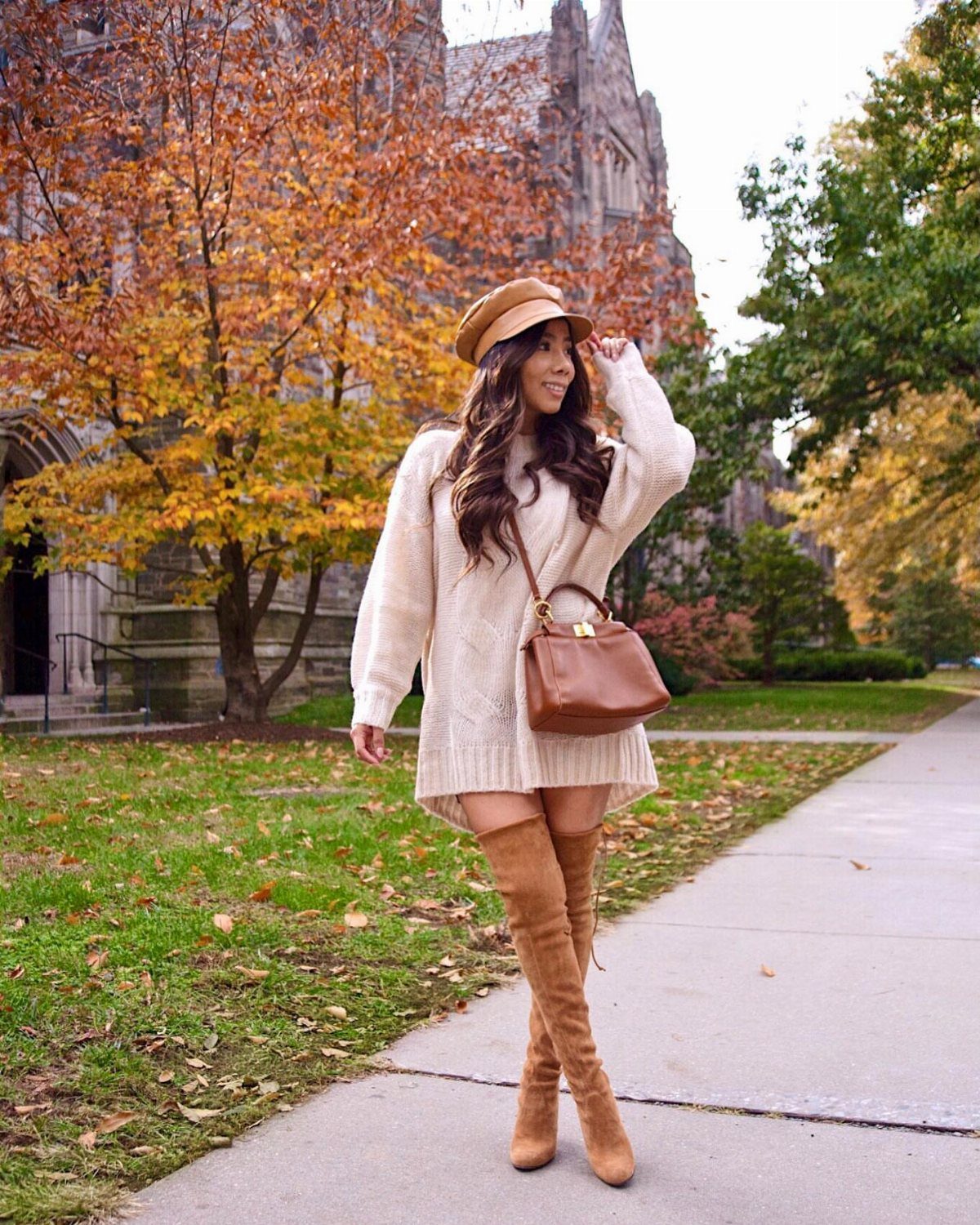 Woman in white knit sweater dress and brown boots posing in autumn setting