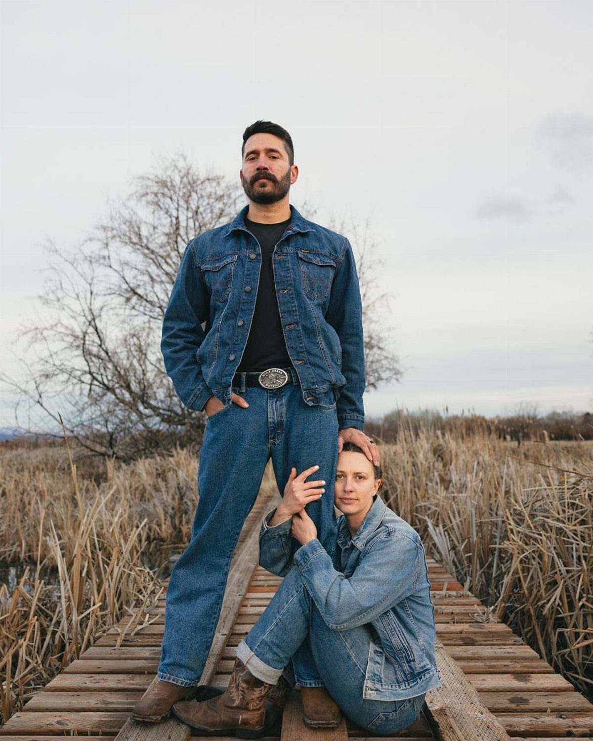 Couple in denim outfits posing on a wooden boardwalk in a fall field