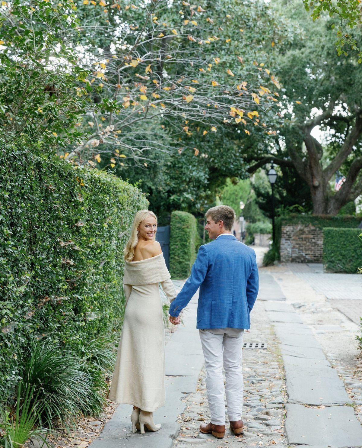 Couple walking on cobblestone path, woman wearing a long cream knit maxi dress.