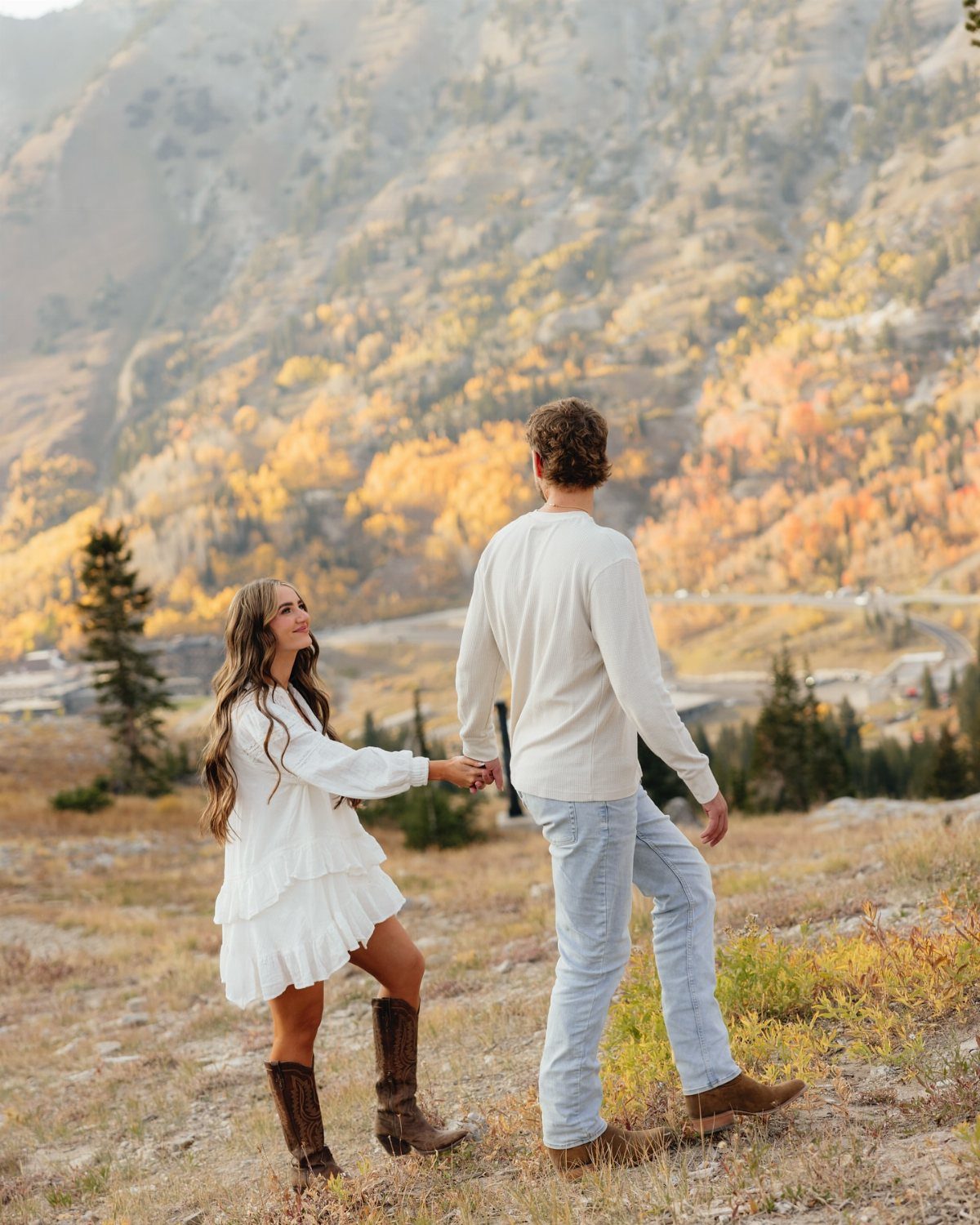 Couple in white and cream autumn outfits holding hands in a mountain landscape