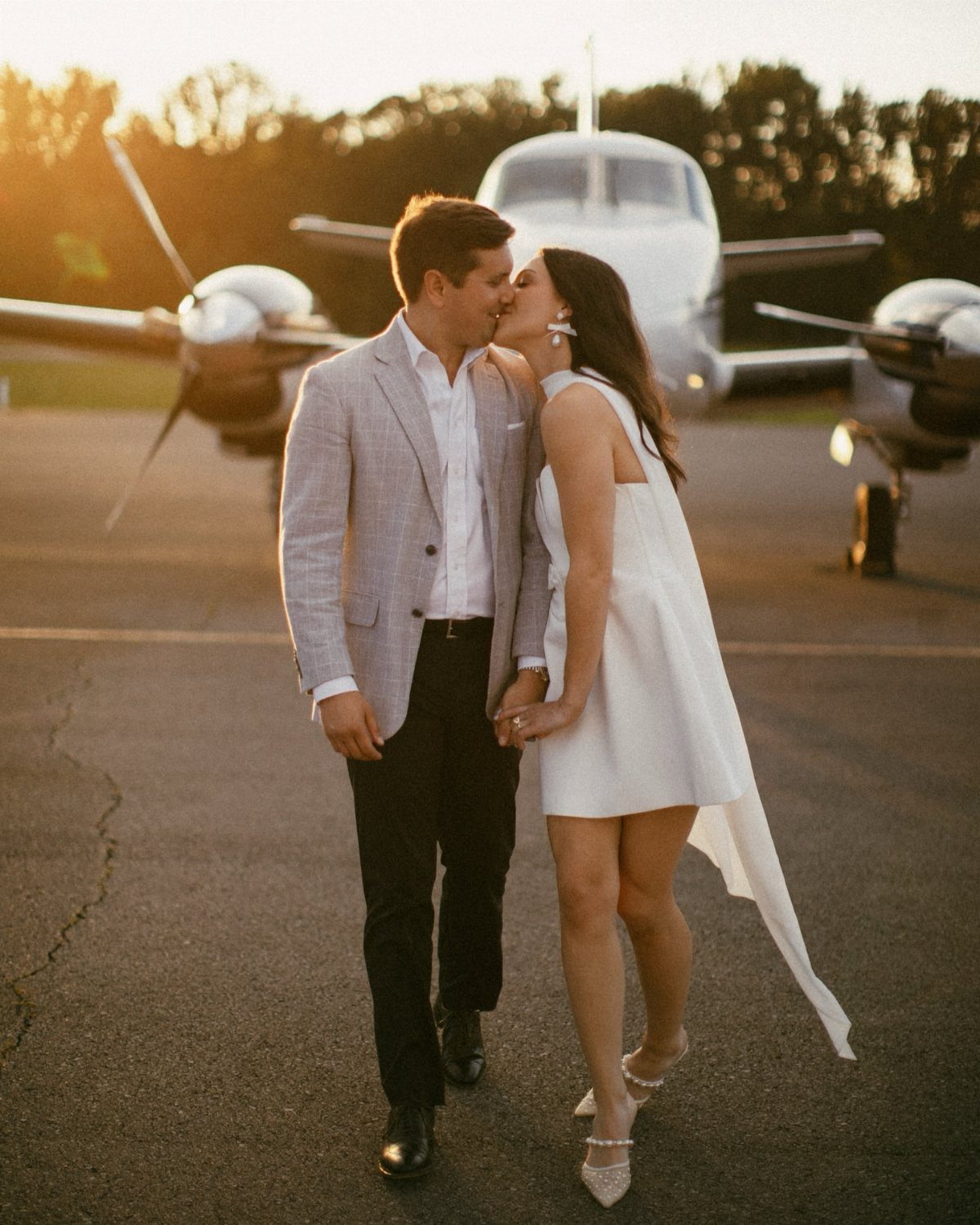 Couple kissing on an airfield in front of a plane during golden hour.