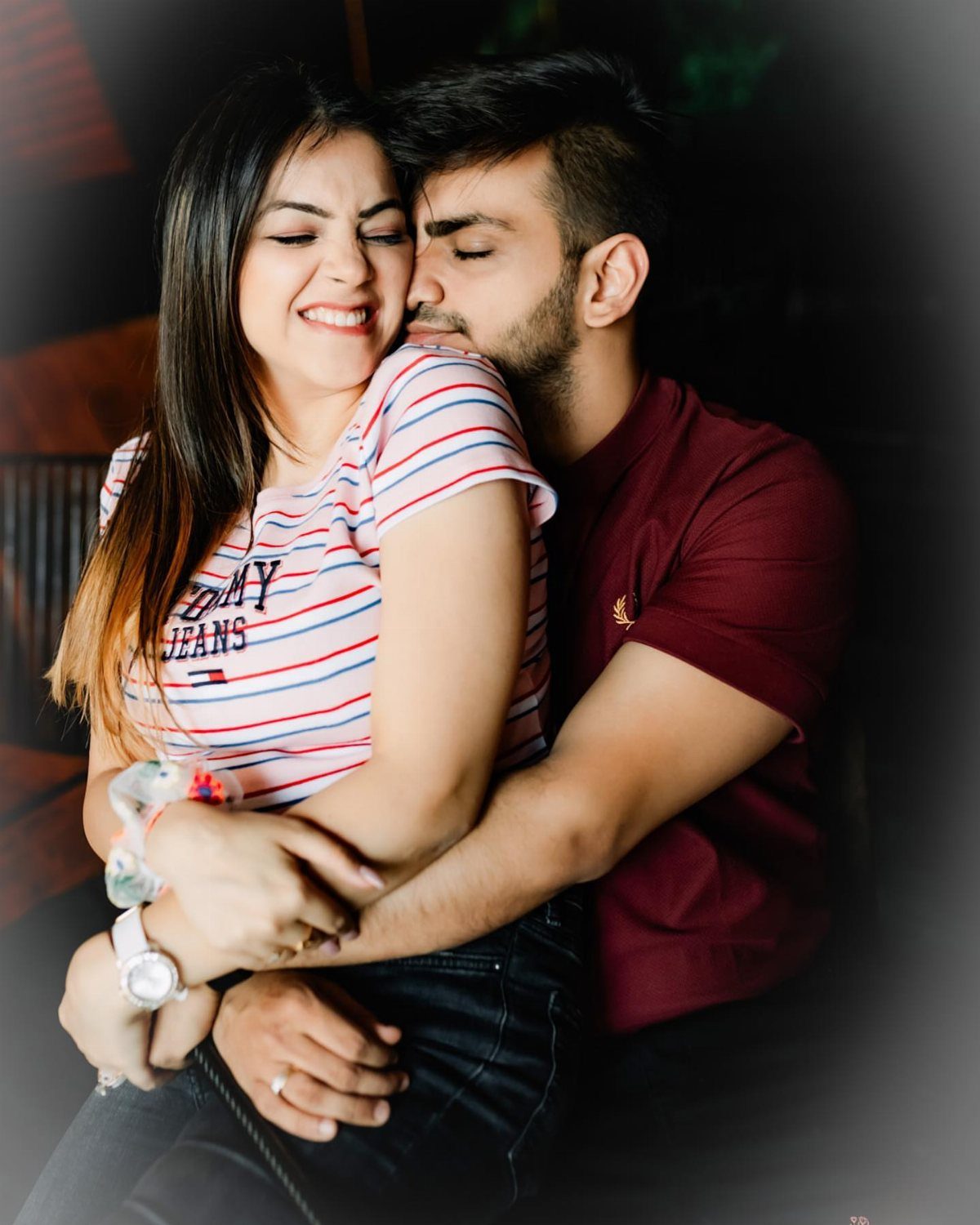 Man hugging woman from behind while she smiles with eyes closed indoors.