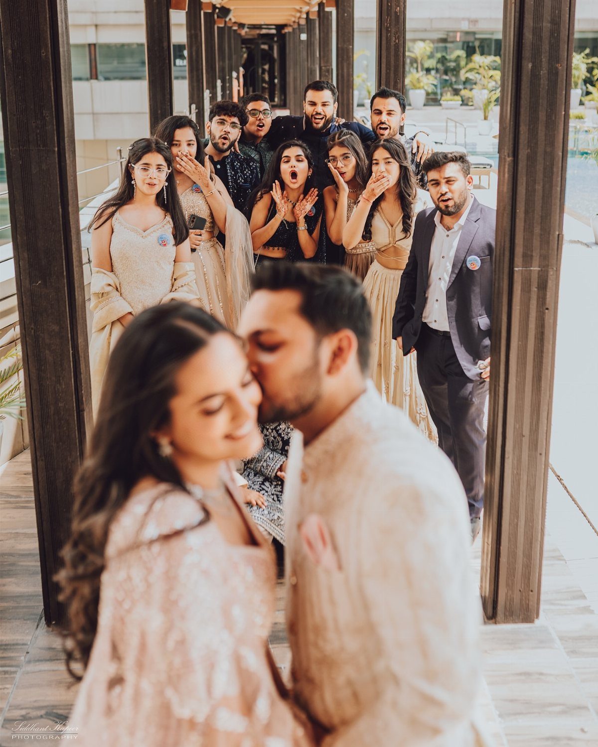 Couple embracing and kissing while friends react with surprise in the background.