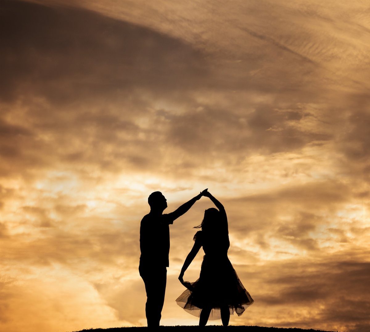 Silhouetted couple dancing and twirling against a golden sunset sky with clouds.