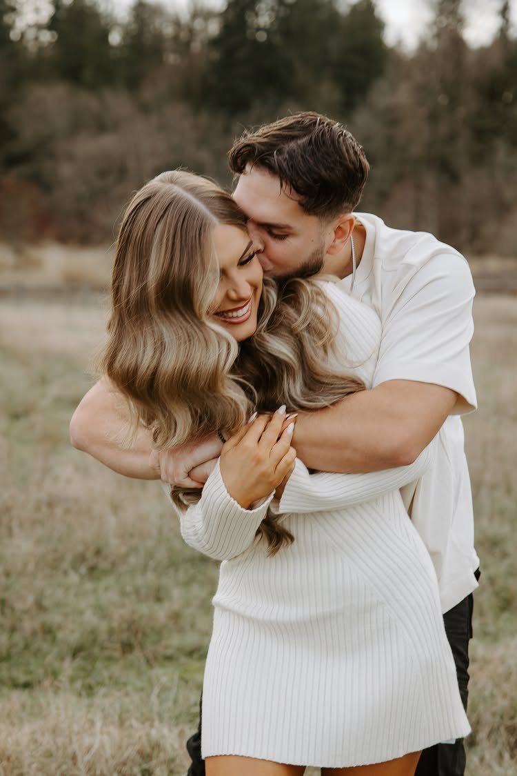 Couple embracing in a field, woman in a white knit dress and man in white shirt.