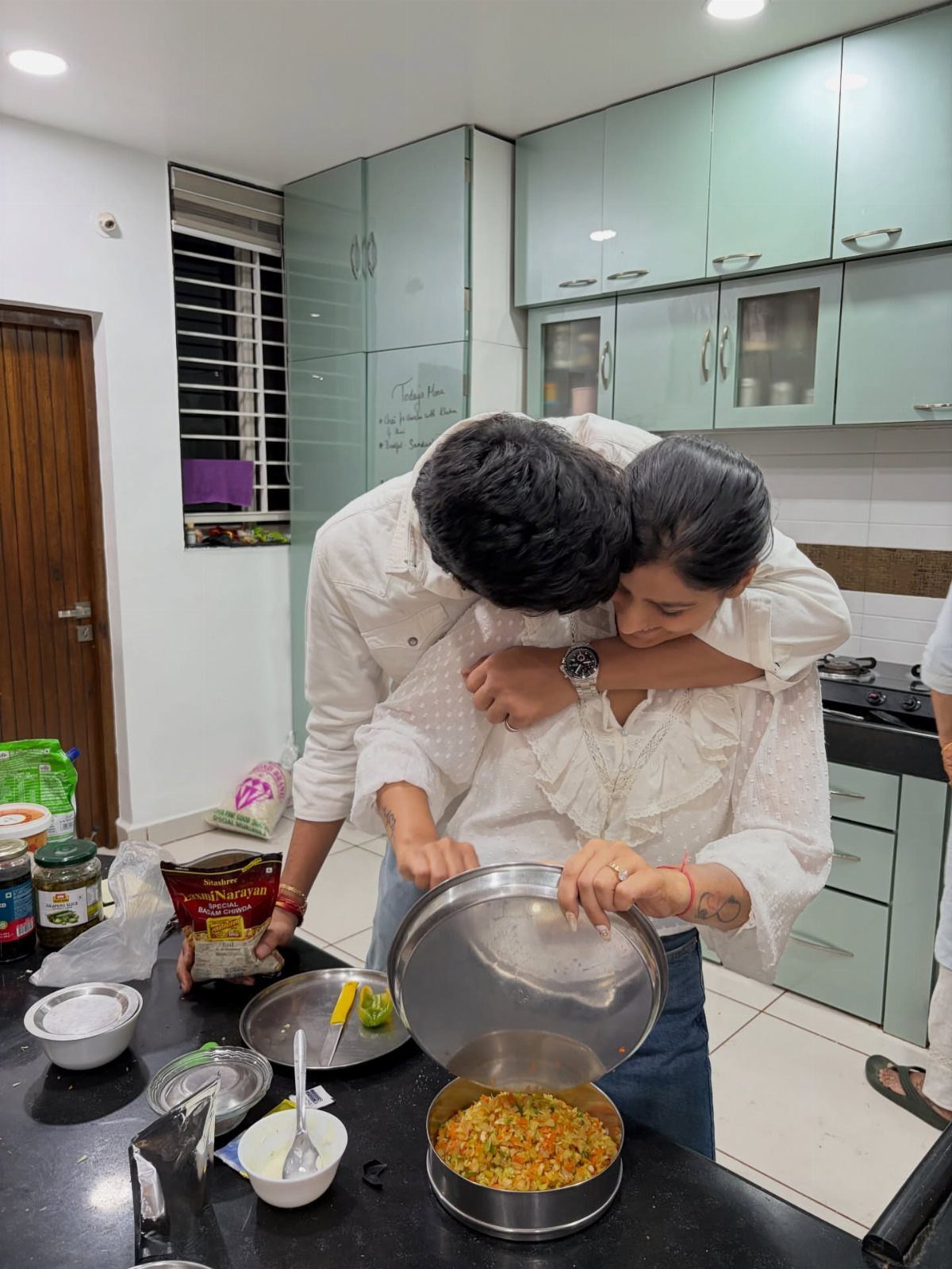 Couple hugging in a kitchen while looking at a pot of food together.