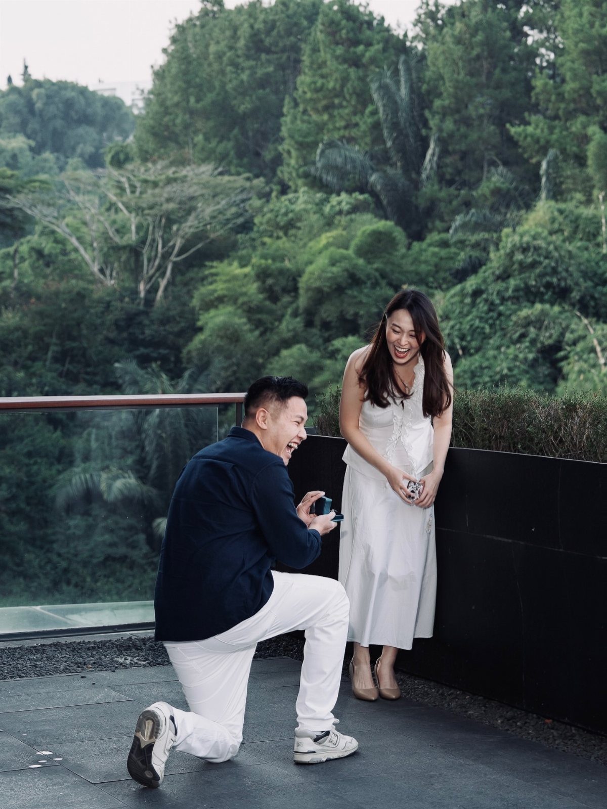 Man kneeling on one knee proposing to a woman on a scenic balcony.