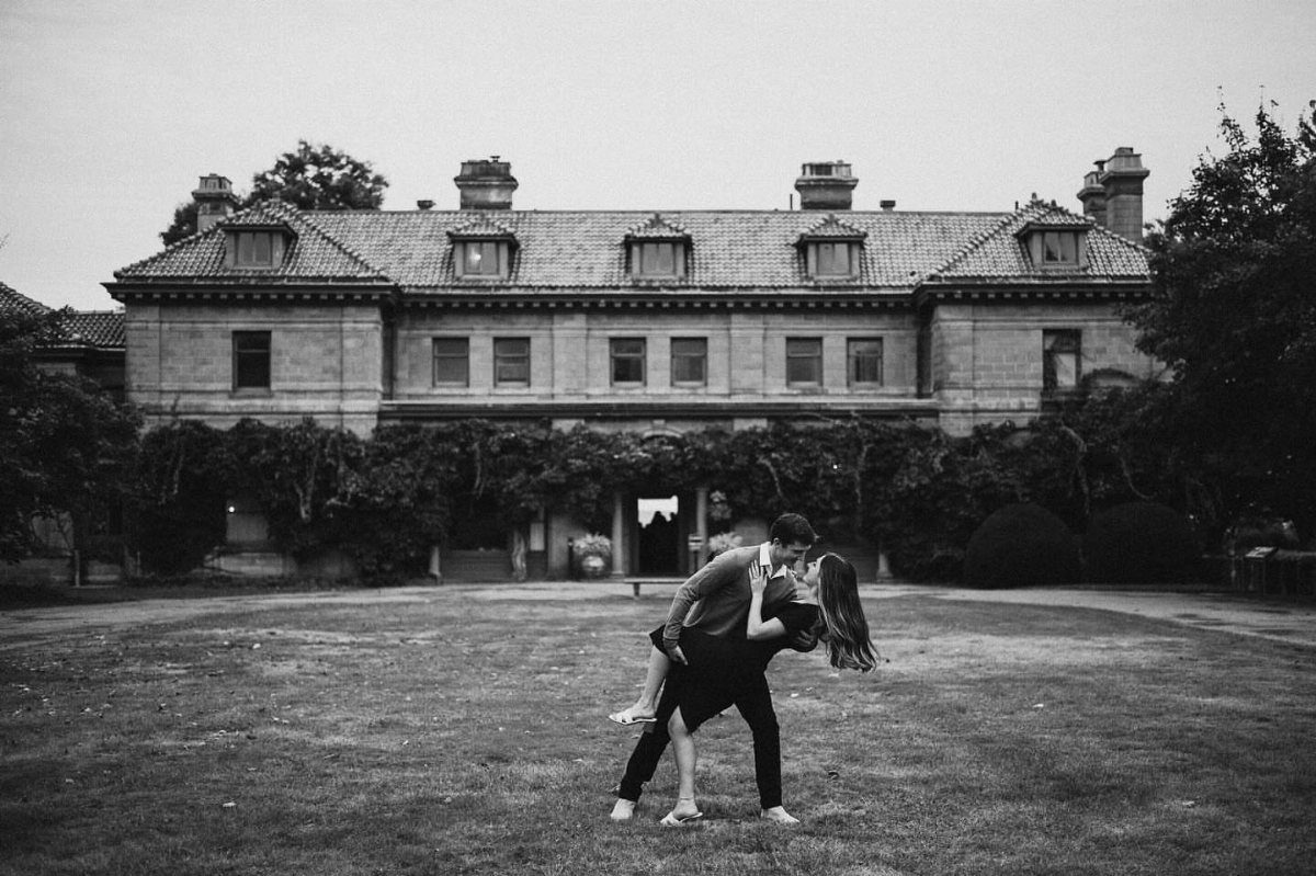 Couple kissing in a dramatic dip pose in front of a large stone mansion.