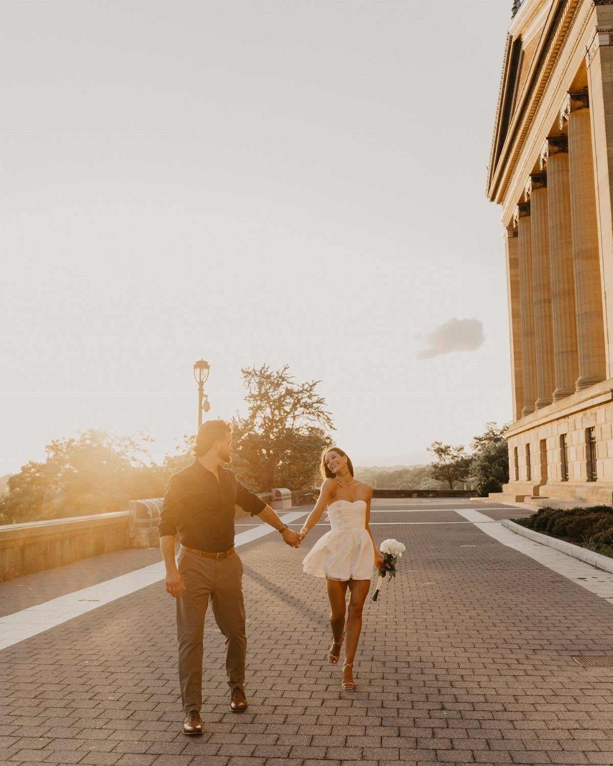 Couple holding hands and walking on a cobblestone path during golden hour.