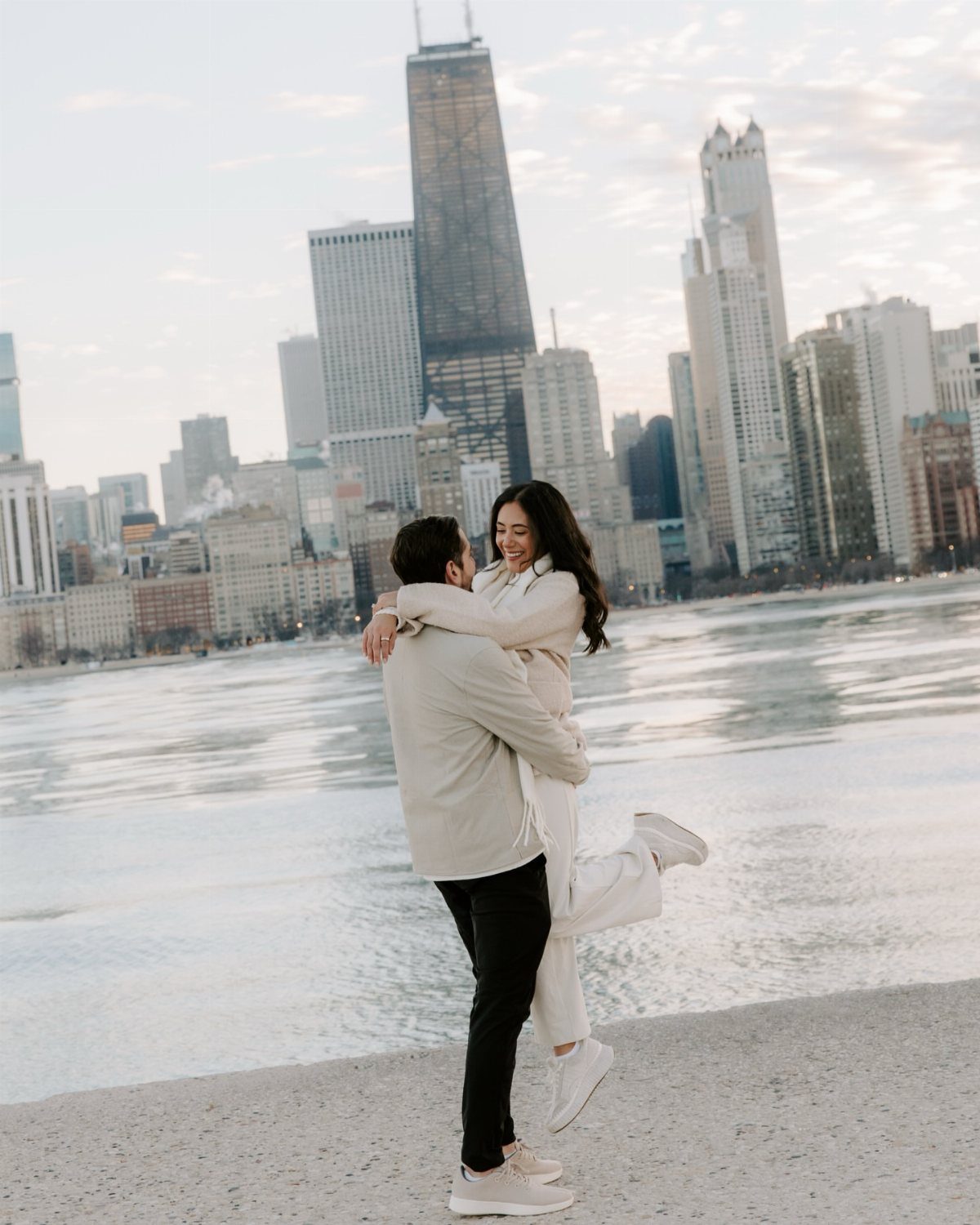 Couple hugging and lifting each other on a waterfront with city skyline background