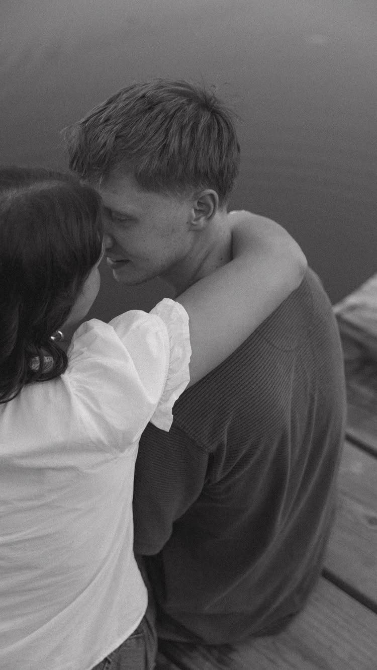 Couple sitting on a wooden dock leaning in close and touching noses.