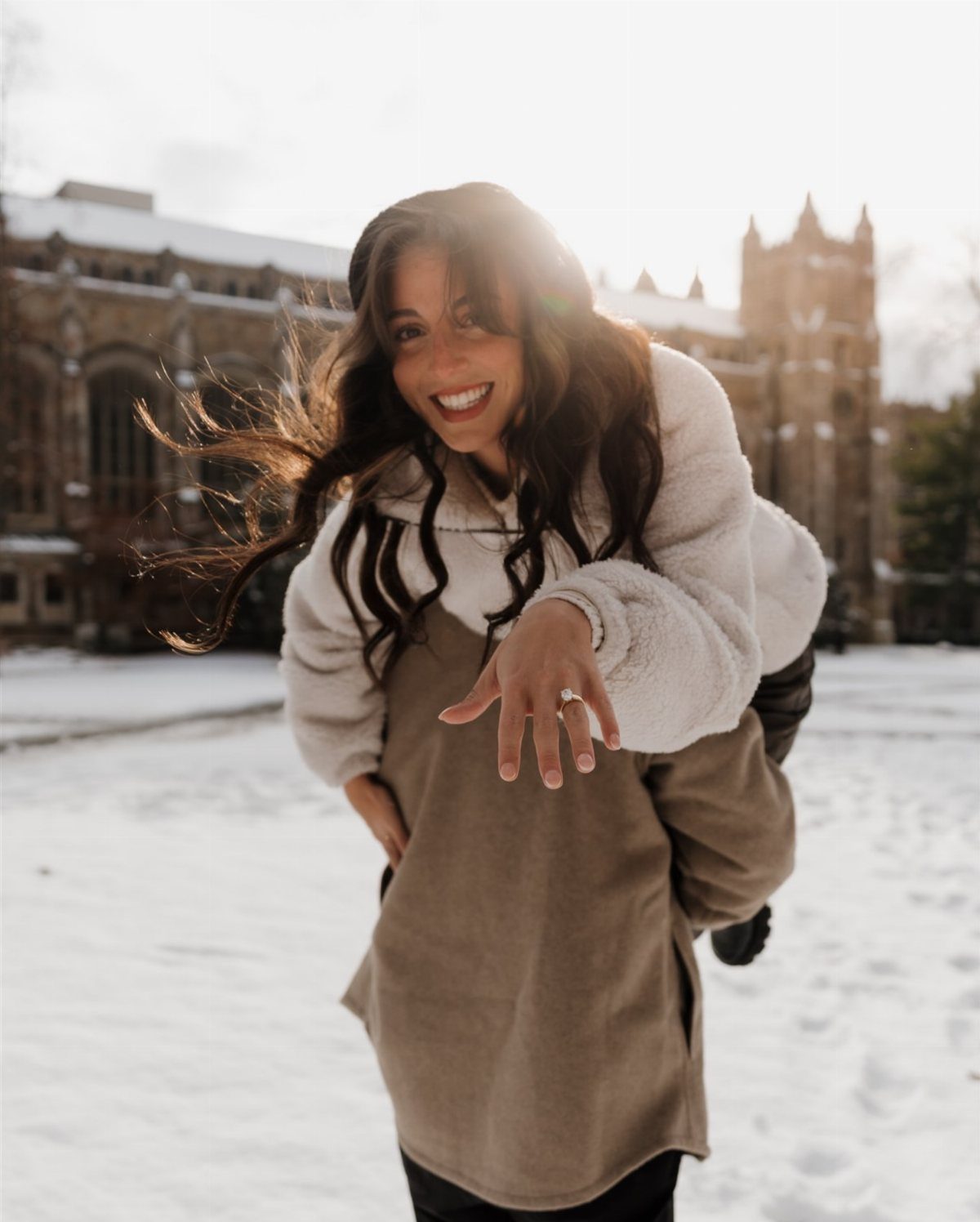 Smiling woman on a man's back showing her engagement ring in the snow