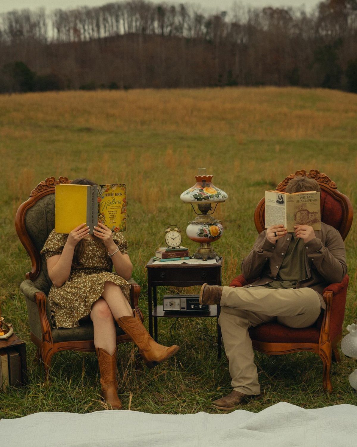 Couple sitting in vintage armchairs in a field reading books over their faces