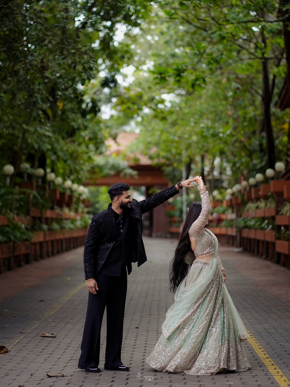 Couple dancing on a tree-lined path with the woman spinning in a lehenga