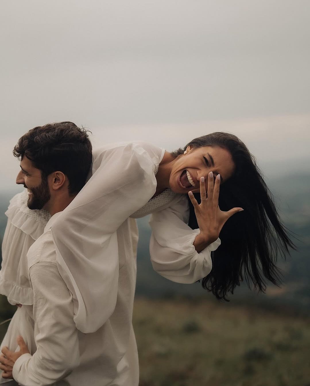 Laughing couple in white clothing posing outdoors in a grassy field