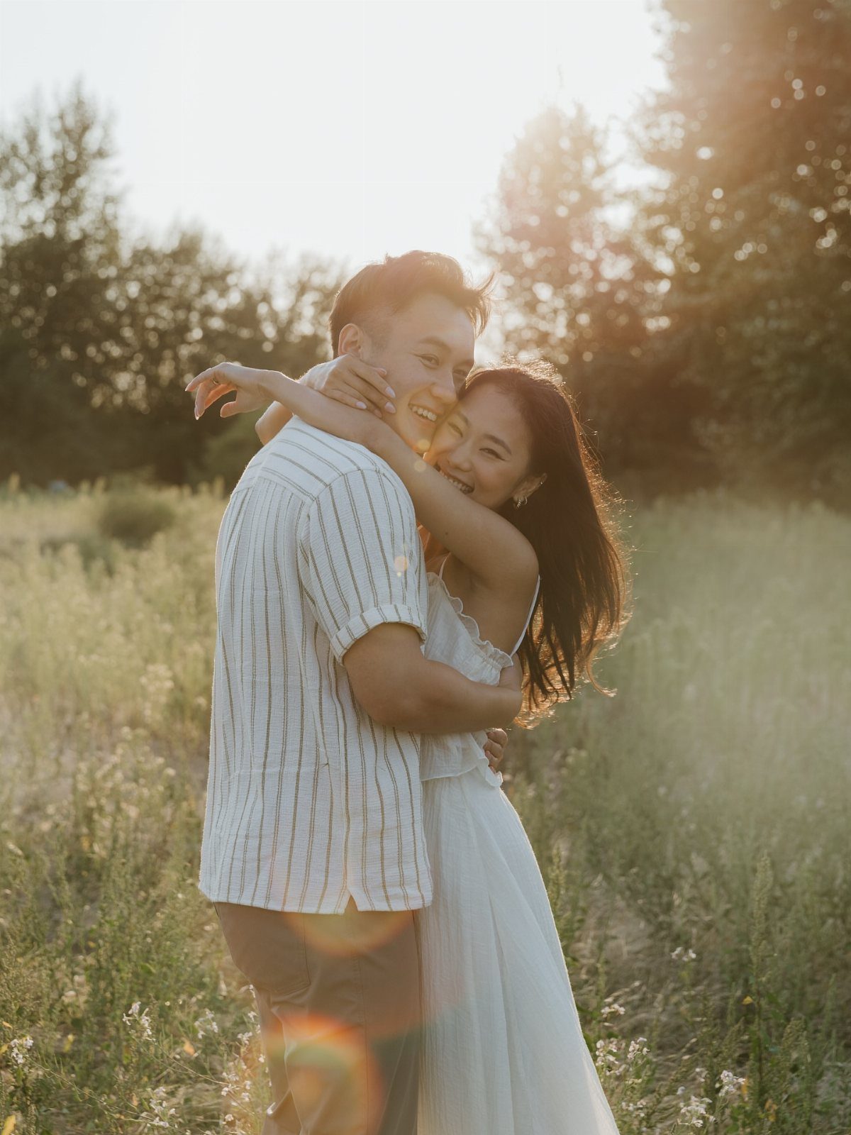 Couple embracing and smiling in a sunlit field during an engagement photo shoot.