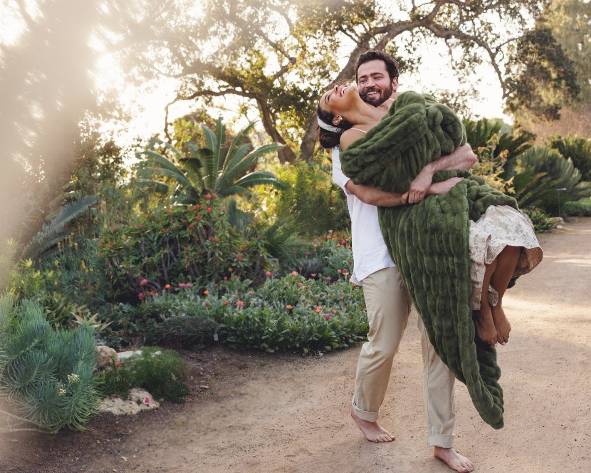 Man carrying a woman wrapped in a green blanket in a sunny garden