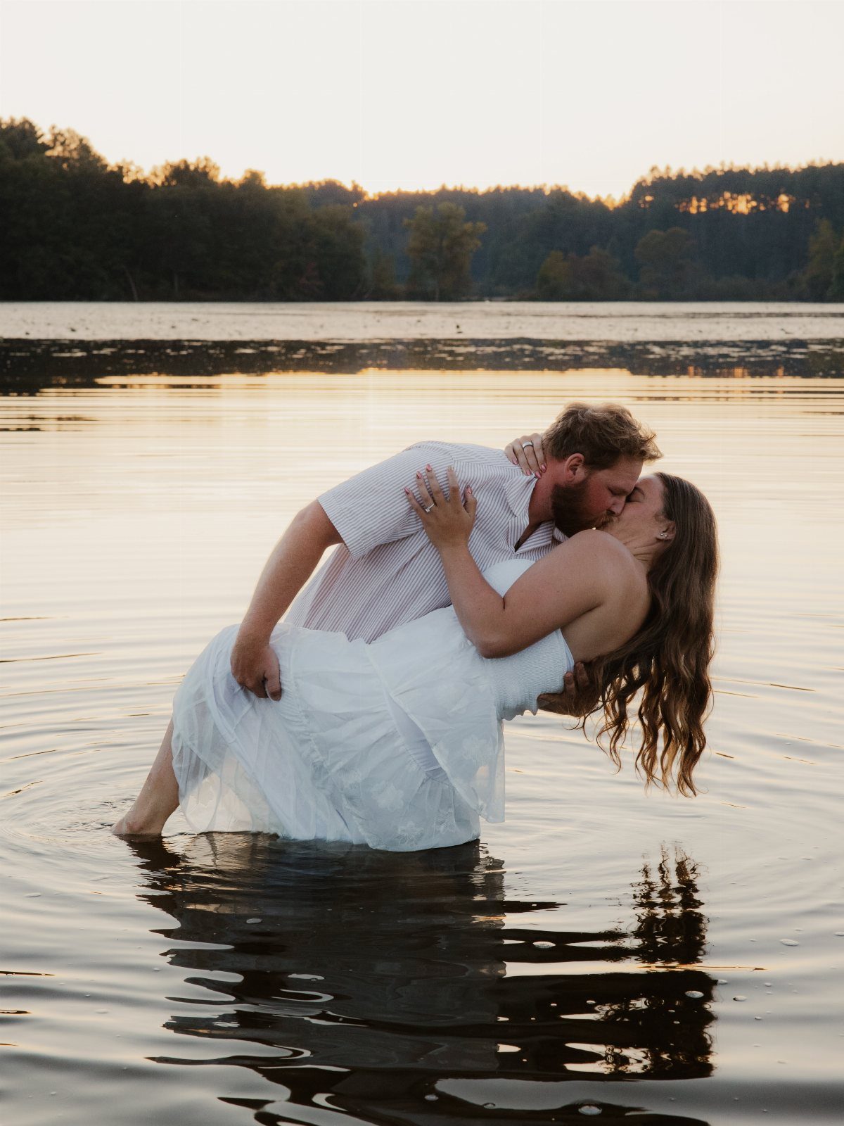 Couple kissing in a lake as the man dips the woman backward.
