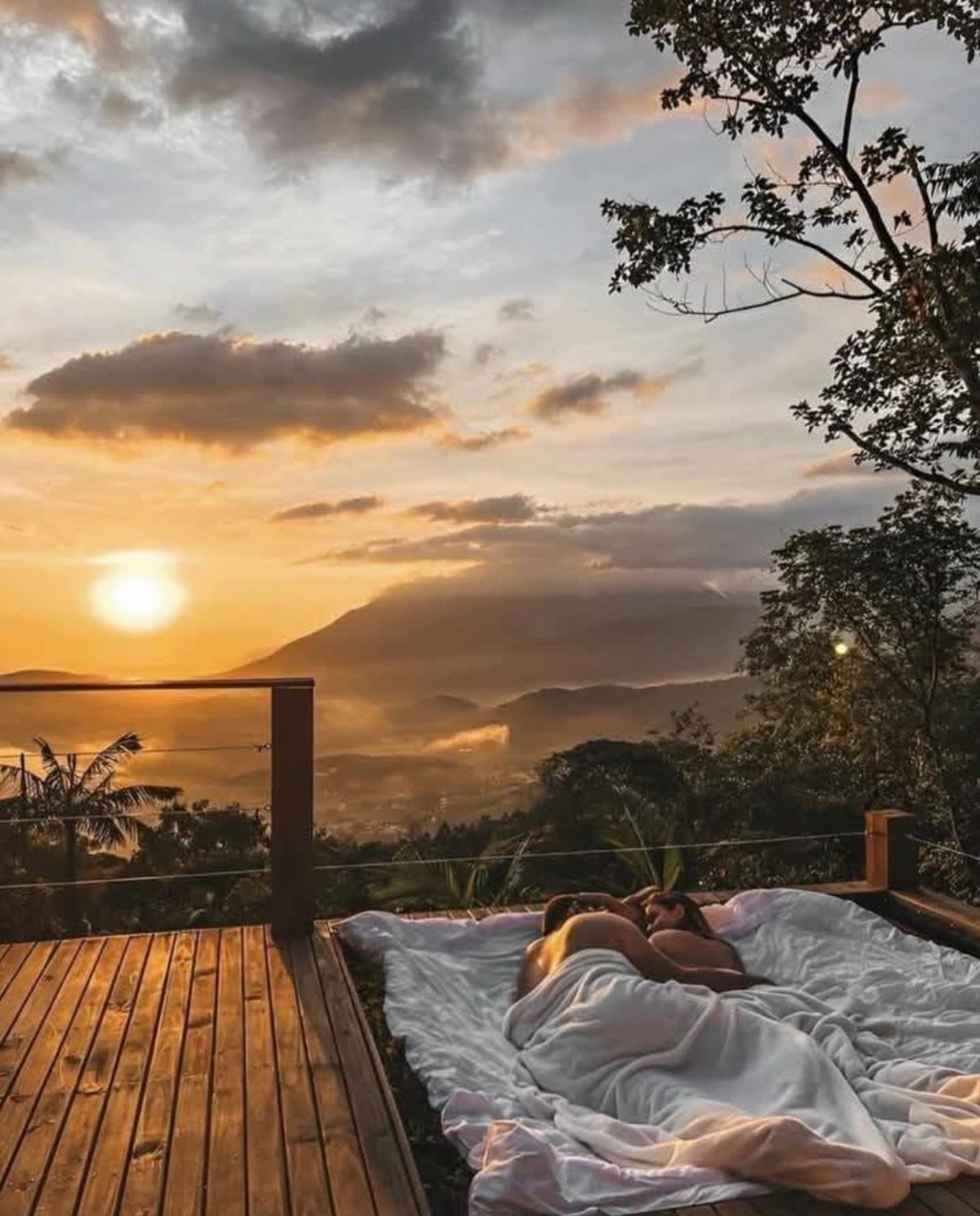 Couple lying on a white blanket on a wooden deck at sunset overlooking mountains