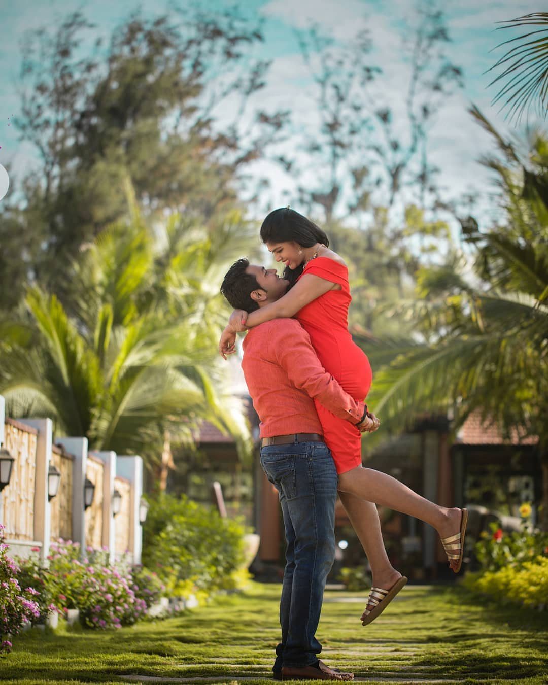 Man lifting woman in a red dress in a tropical garden setting.