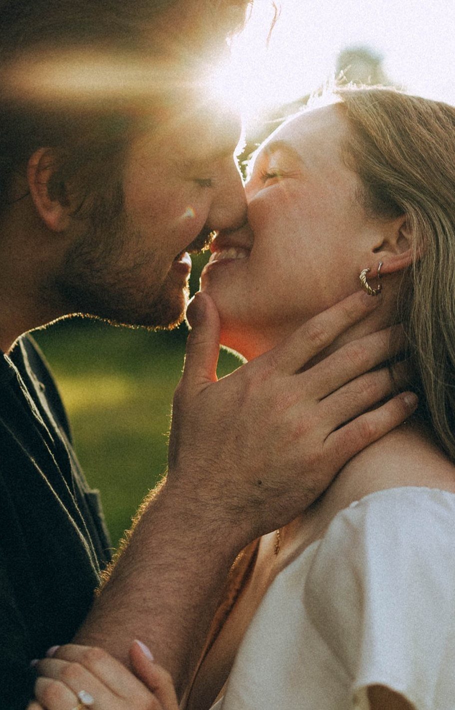 Couple smiling with noses touching in a sunlit outdoor setting during a photoshoot.
