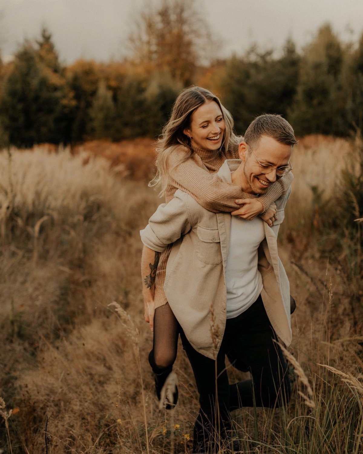 Smiling couple in a field with the woman giving the man a piggyback ride.