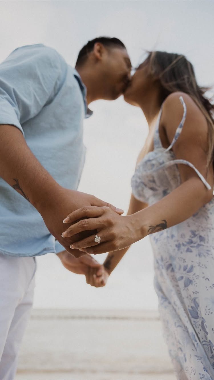 Couple kissing while holding hands, showcasing an engagement ring on the woman's finger.