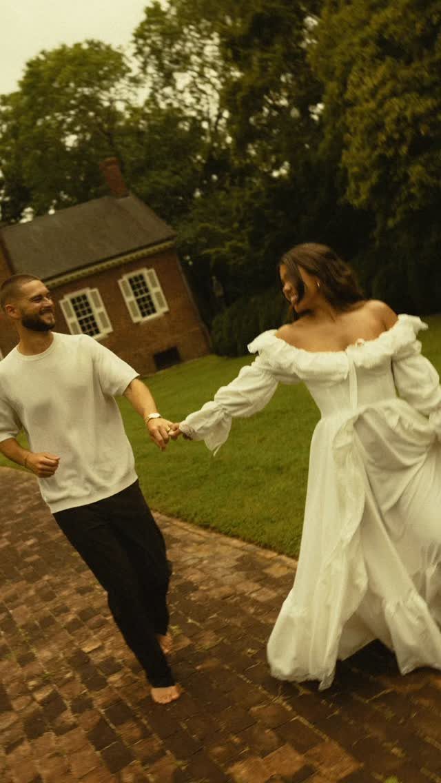 Man spinning a woman in a white dress on a brick path outdoors.