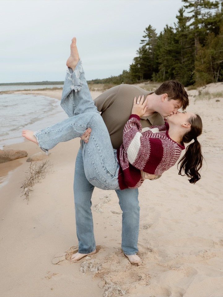 Couple kissing on a sandy beach, man carrying woman in his arms.