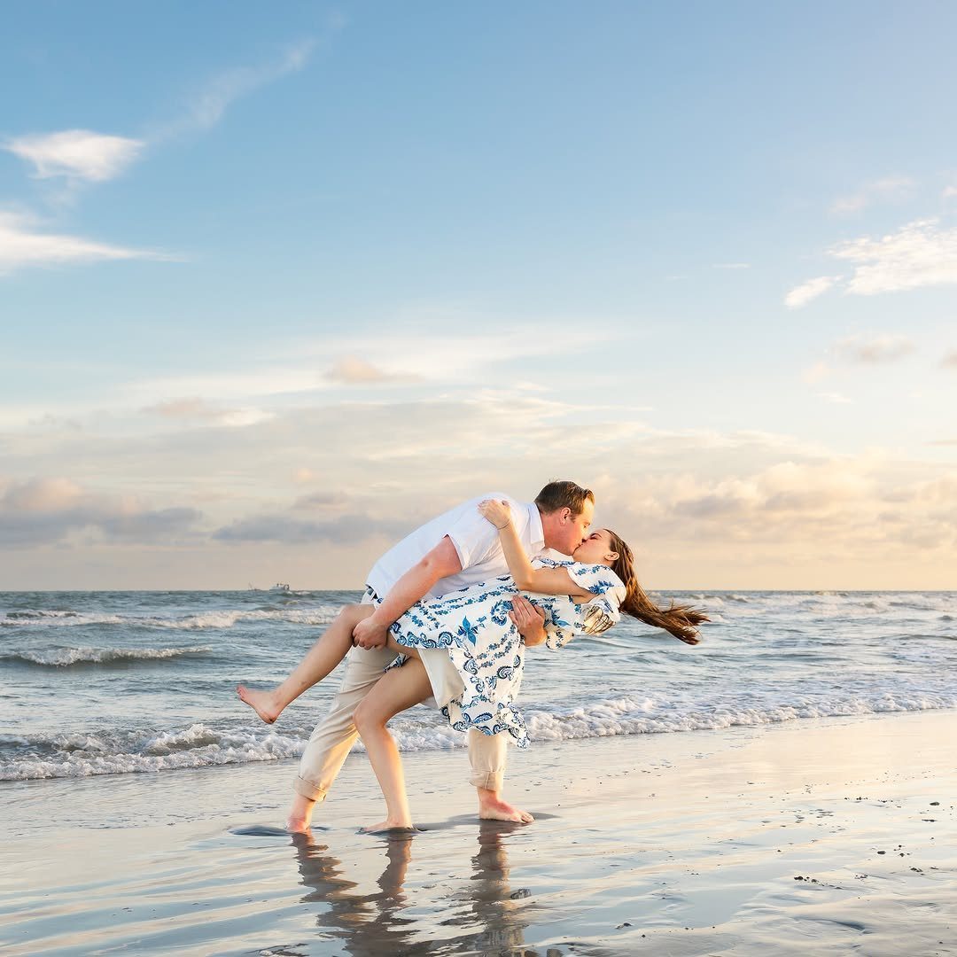 Couple kissing on a beach with the man dipping the woman in the surf.
