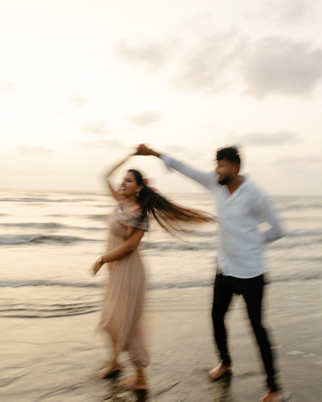 Couple dancing on a beach at sunset with motion blur and soft lighting.