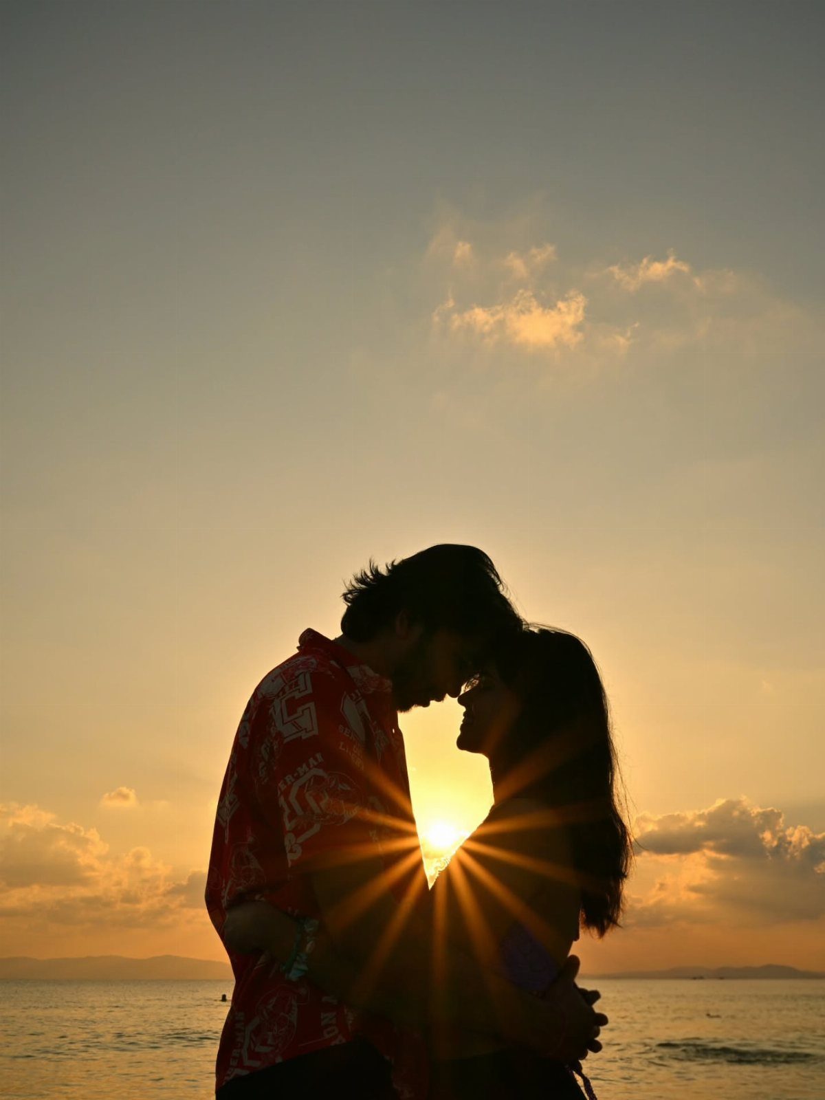 Couple in silhouette facing each other with the setting sun between their faces.