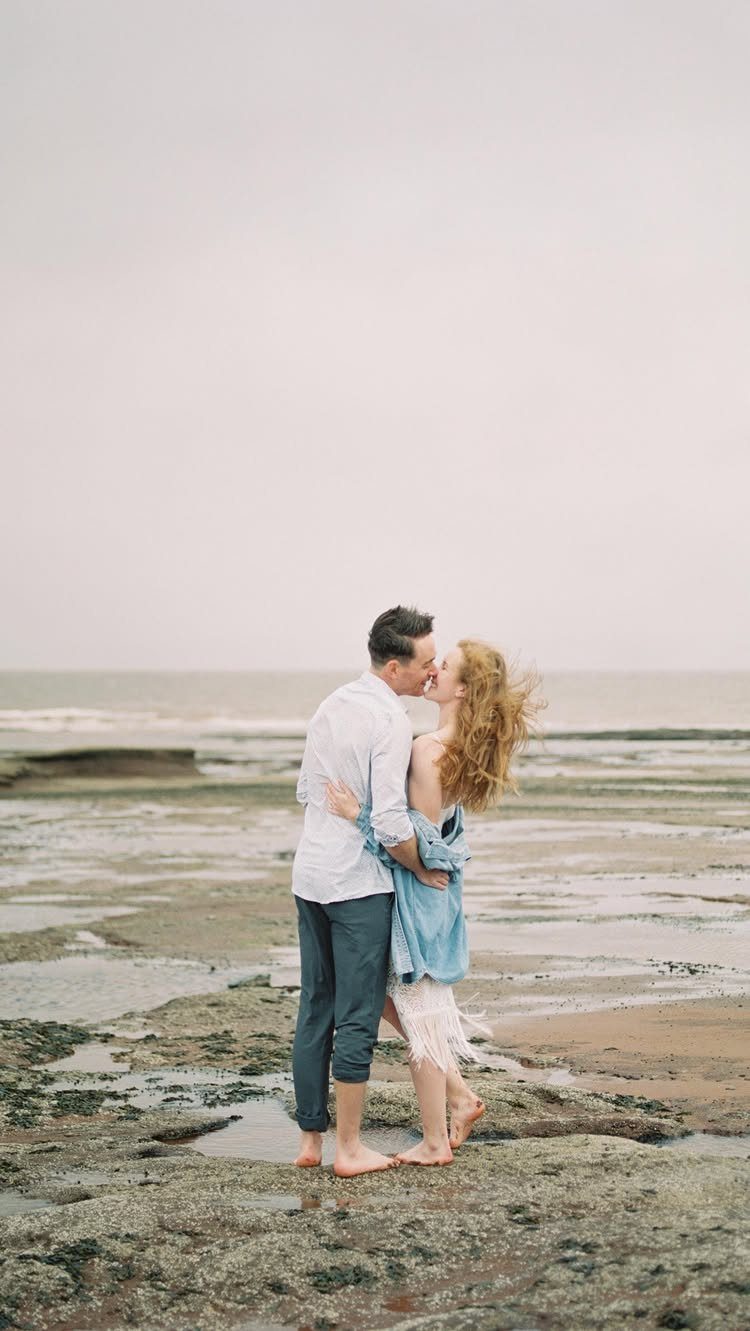Couple kissing while standing in shallow tide pools on a rocky beach.