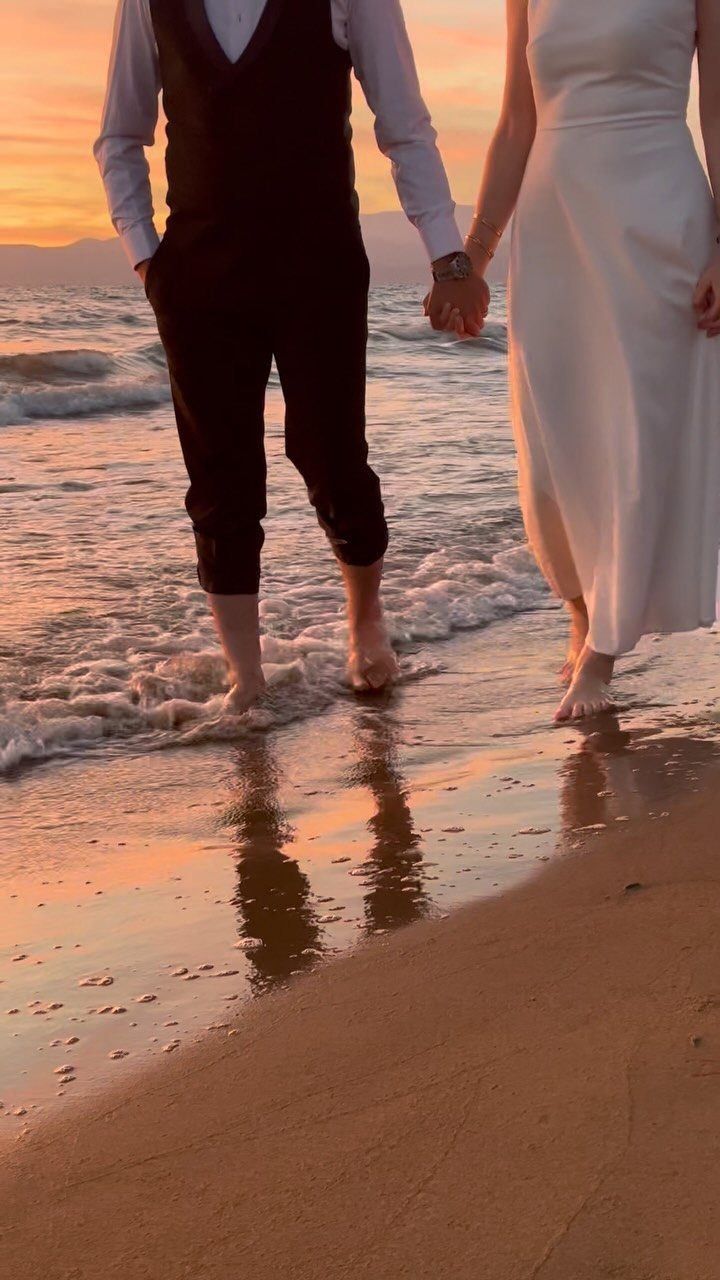 Couple holding hands walking barefoot along the shoreline during a golden sunset.