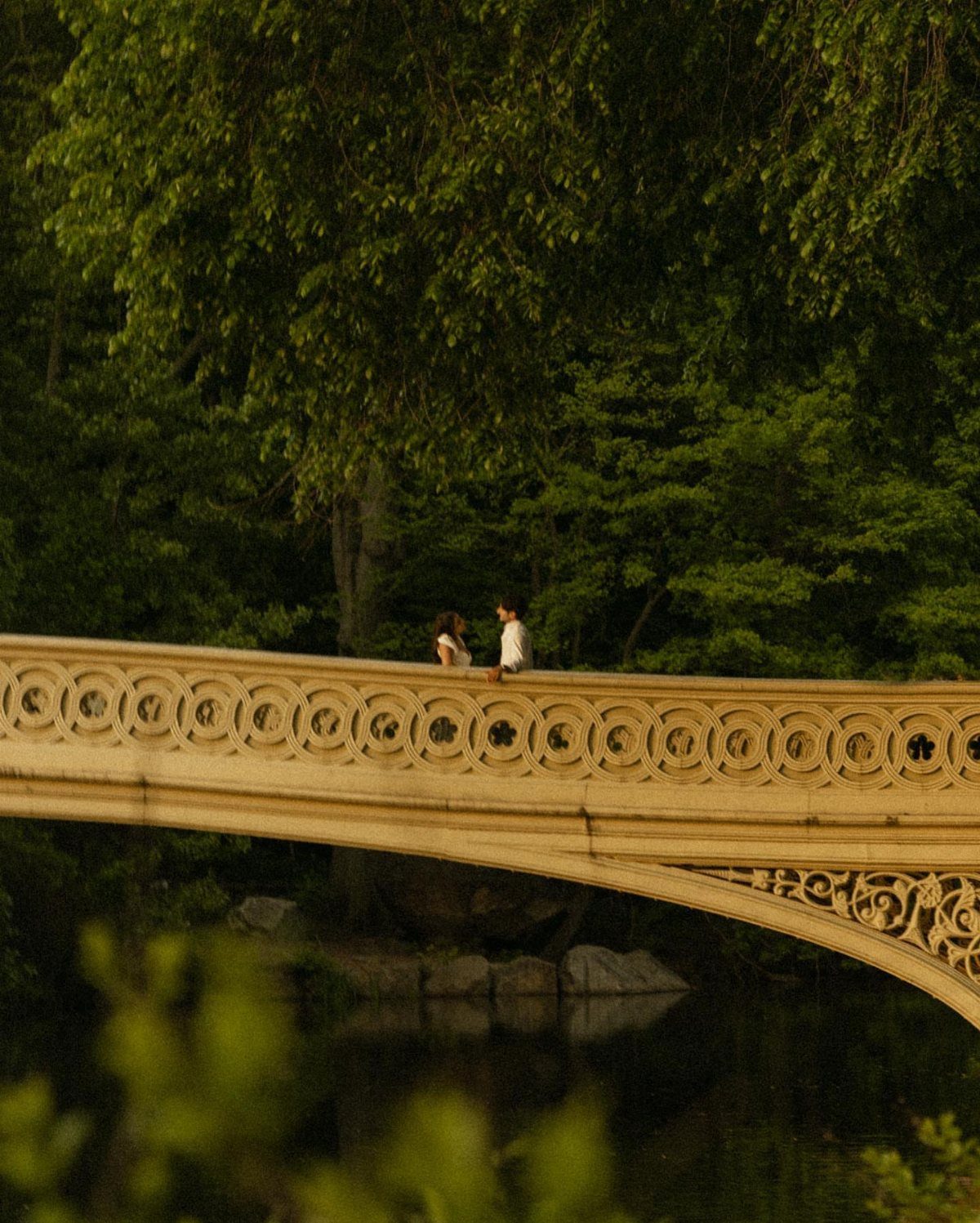 Couple standing on a decorative yellow bridge surrounded by lush green forest trees