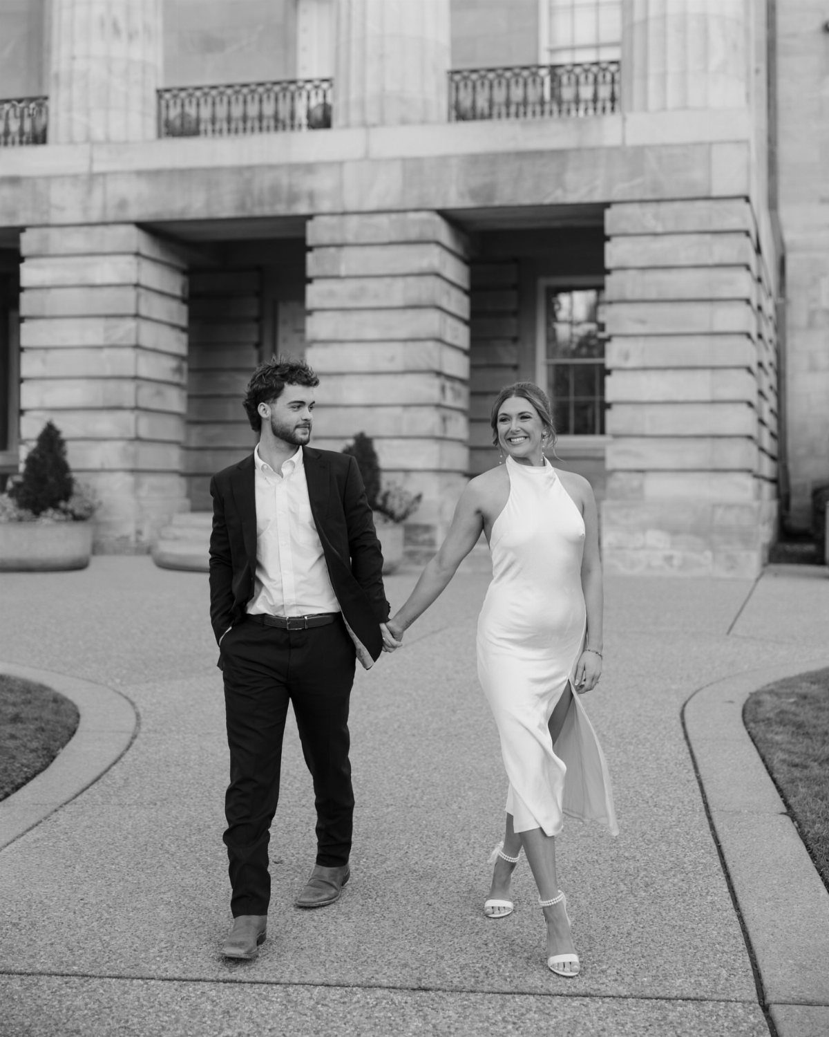 Couple holding hands and walking in front of a historic stone building.