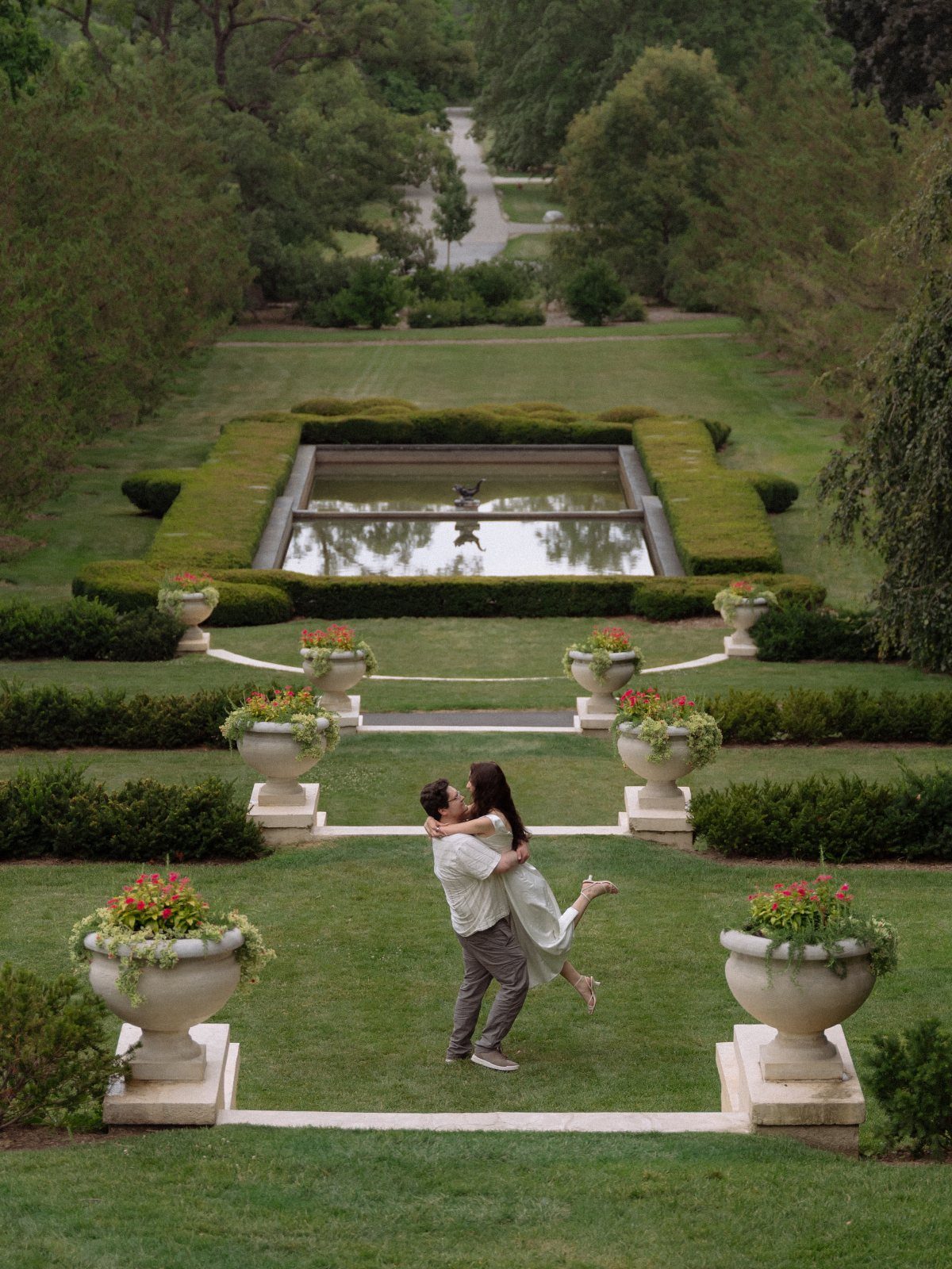 Couple embracing in a formal garden with reflecting pool and manicured hedges.