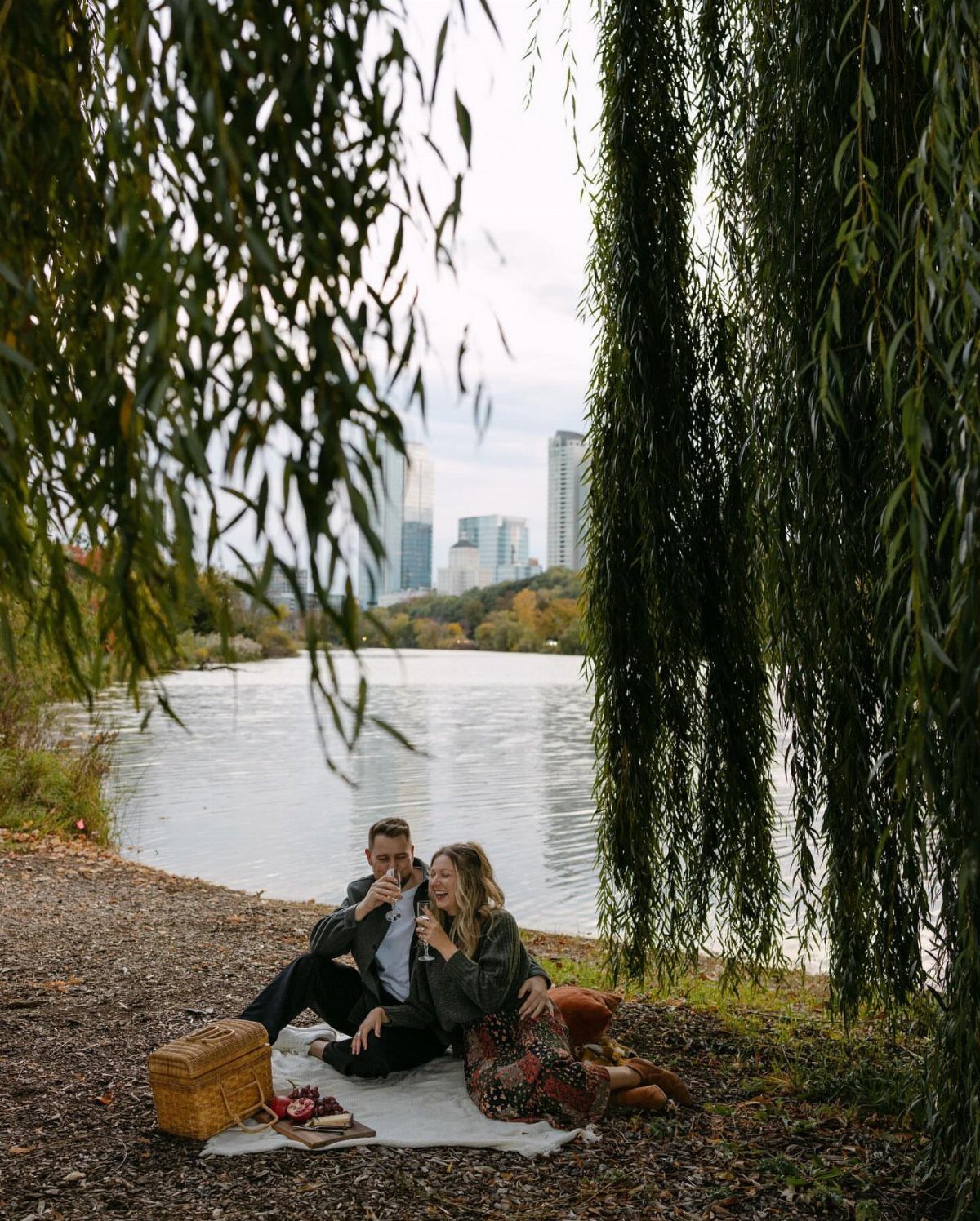 Couple having a picnic by a lake with a city skyline in background