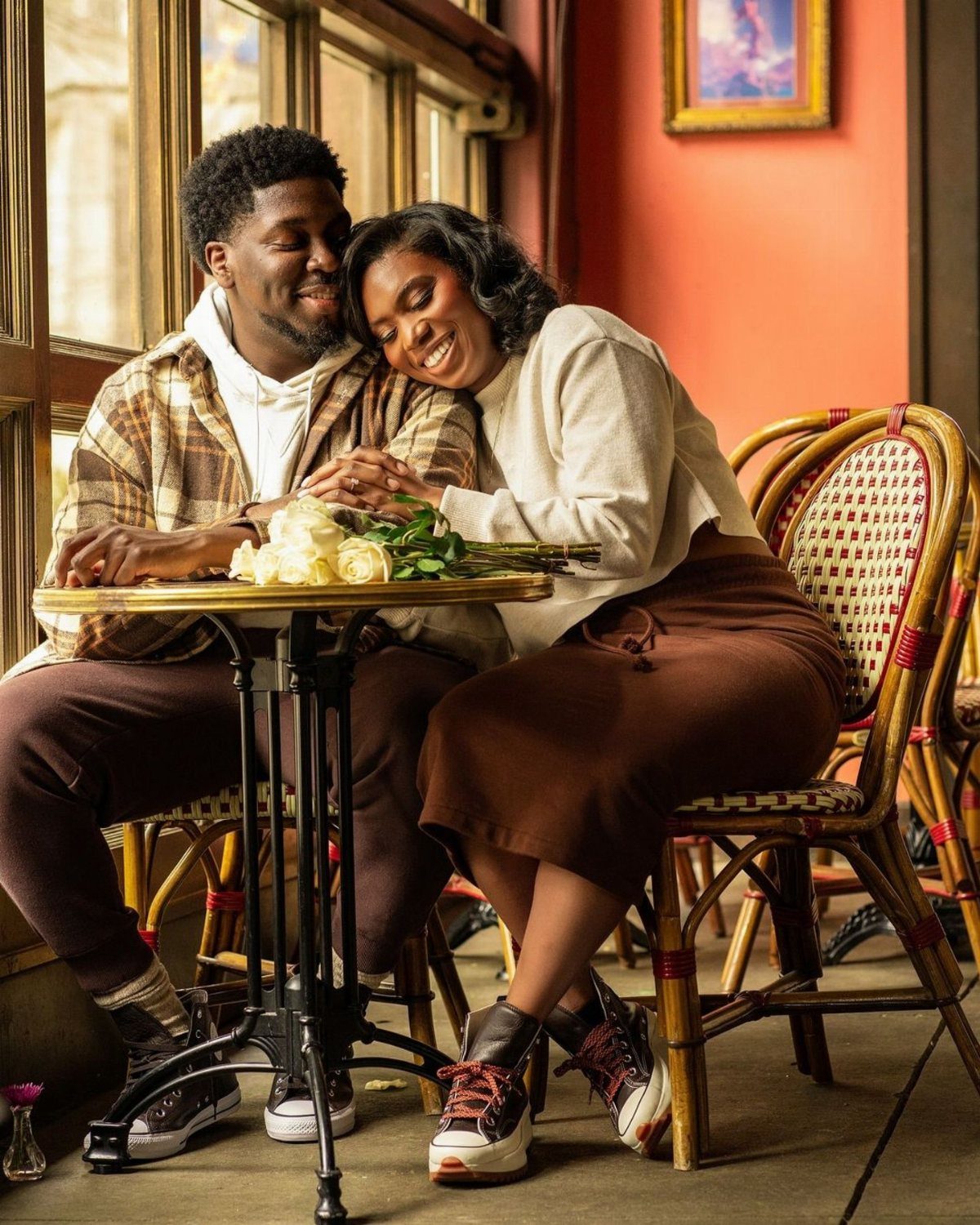 Black couple smiling and leaning into each other at a cafe table with roses.