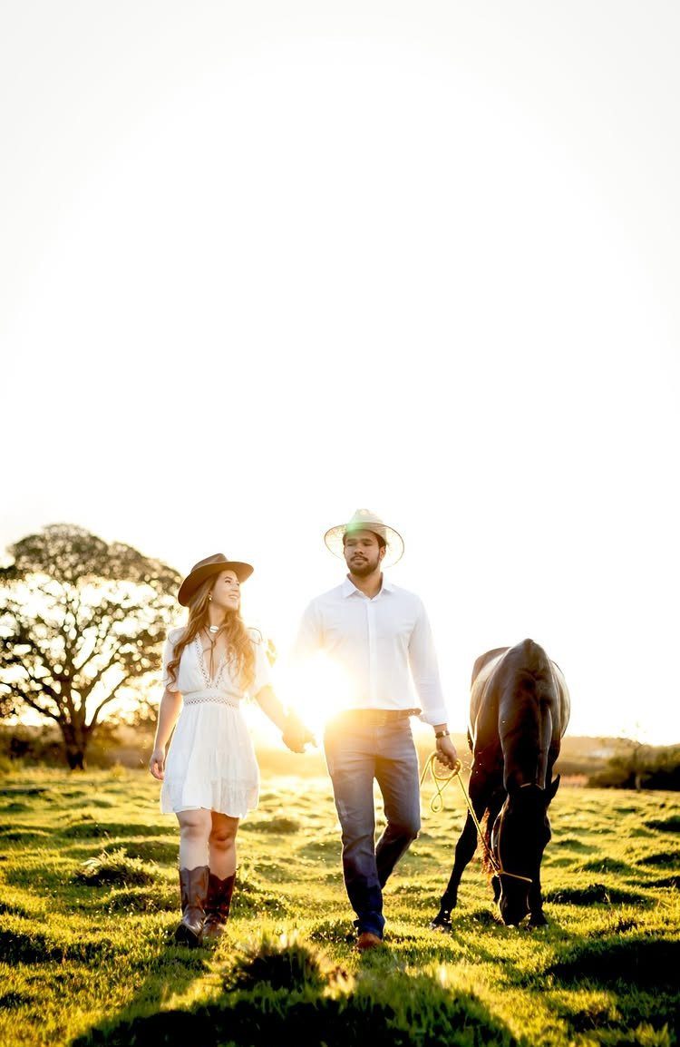 Black couple in western wear walking with a horse in a sunny field