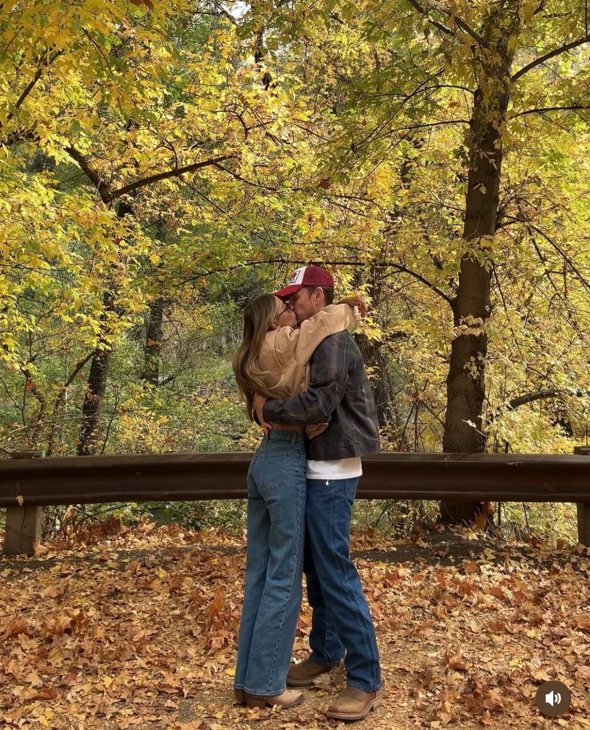 Couple embracing in autumn forest wearing tan and grey jackets with blue jeans
