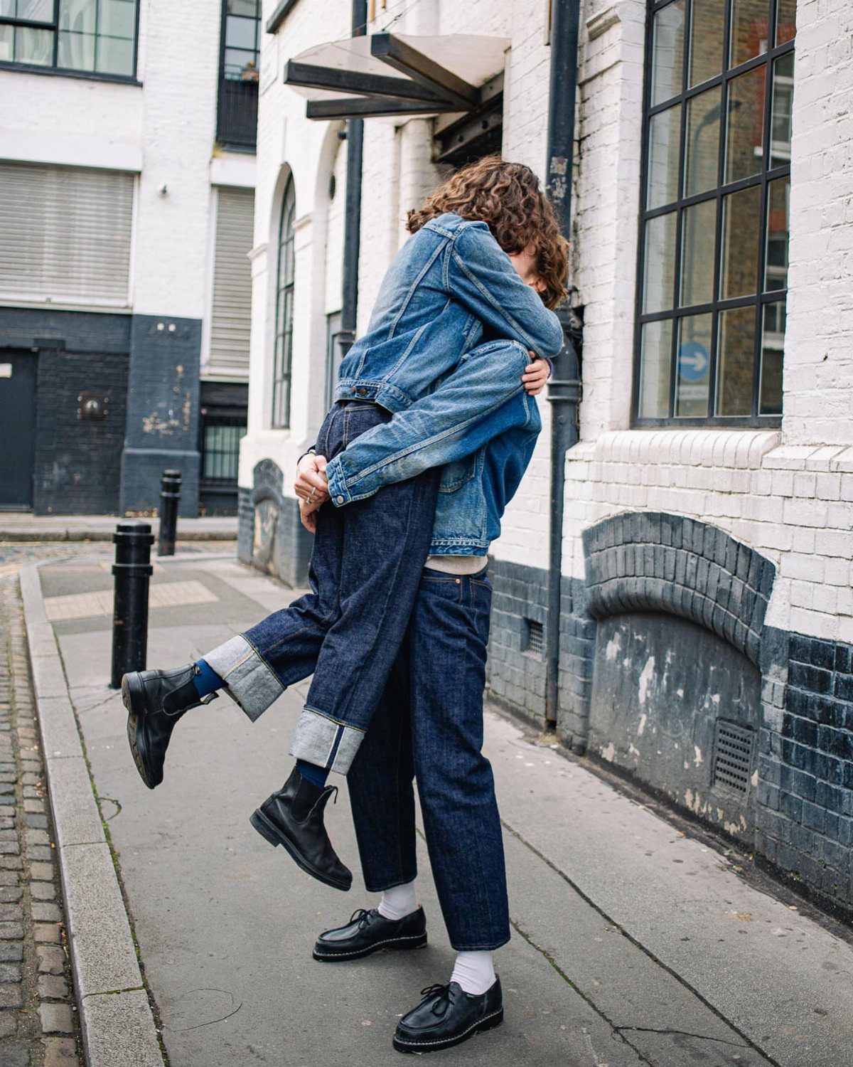 Couple embracing in an alley wearing matching blue denim jackets and jeans.