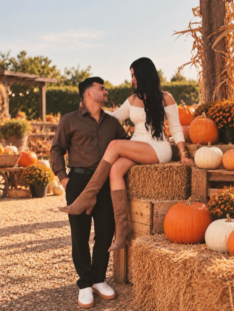 Couple posing in autumn attire at a pumpkin patch with hay bales.