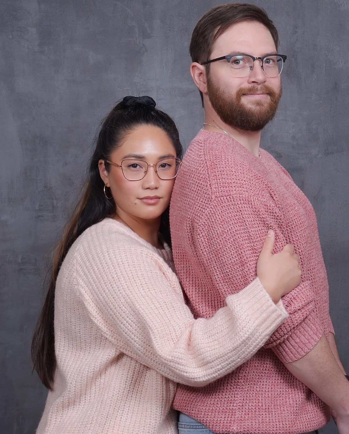 Couple in pink sweaters and glasses posing for an awkward throwback style portrait