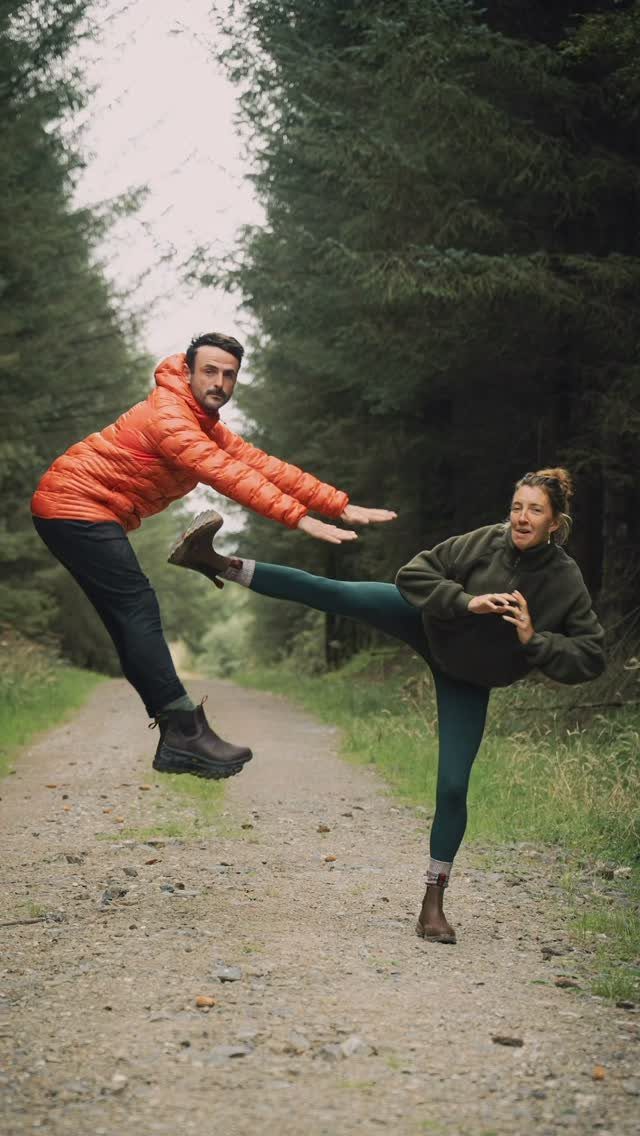 Couple posing playfully on a forest path with woman kicking the man.