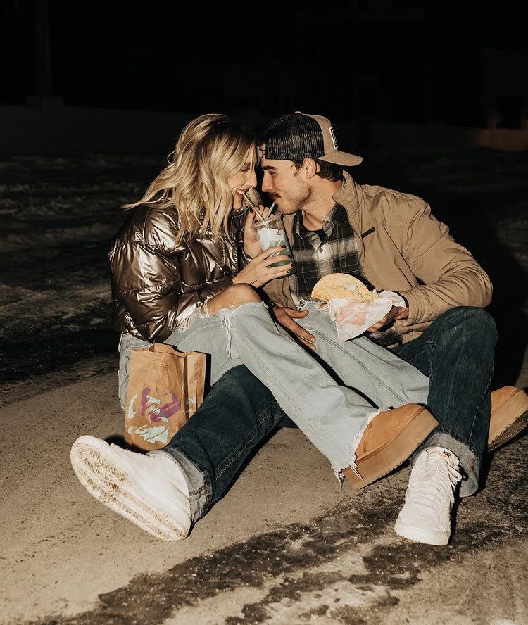 Young couple laughing and eating fast food while sitting on the ground at night.